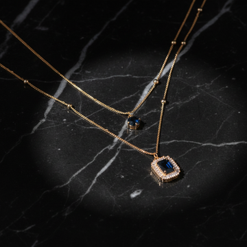 Gold double layer necklace with dark navy stone on dark luxury background