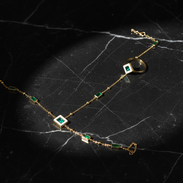 Gold hand chain bracelet ring set with emerald green stones on dark luxury background